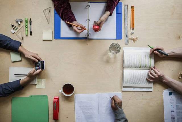 Overhead view of four students working around a table with textbooks, notebooks, a calculator and a ruler