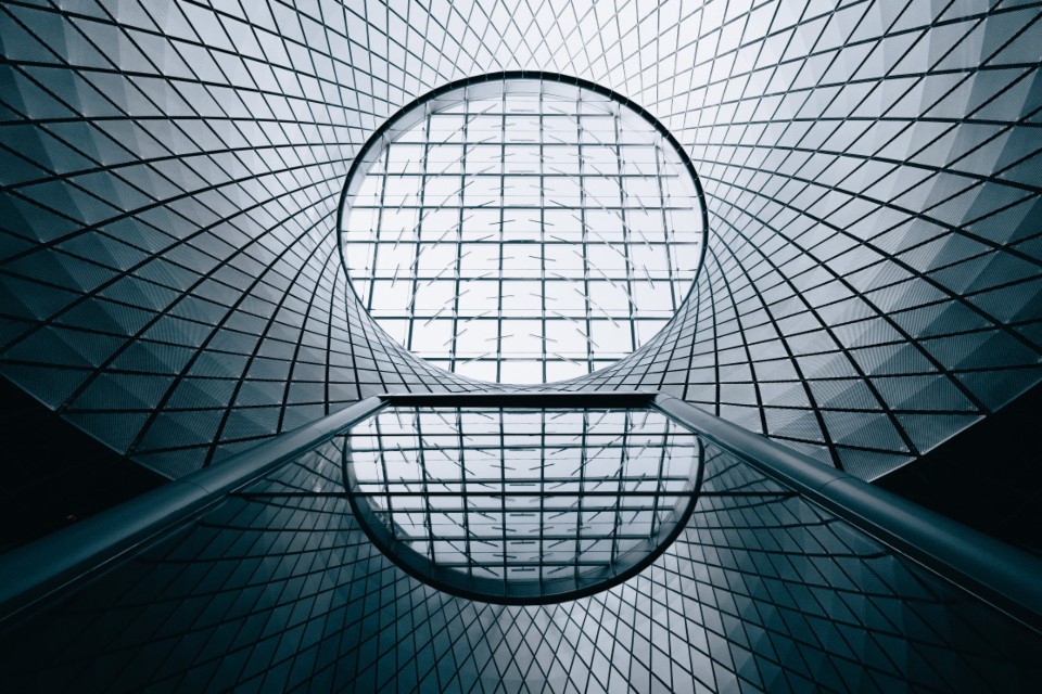A symmetrical glass roof seen from directly below, its circular oculus mirrored in the floor