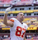 Travis Kelce in his Kansas City Chiefs jersey raising a gloved hand to the crowd in October 2021