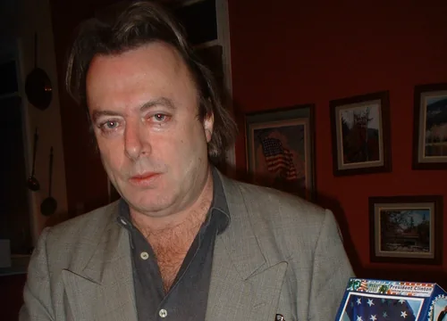 Christopher Hitchens with swept-back brown hair in a gray-green jacket and dark open-collared shirt, looking at the camera in January 2004