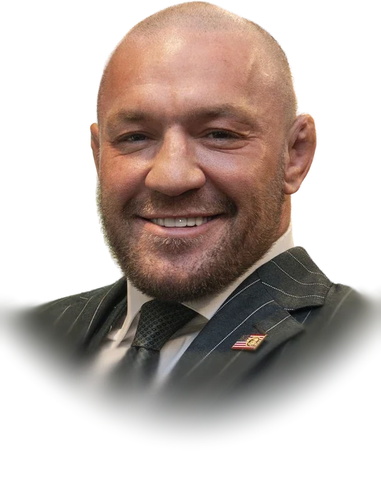 Conor McGregor with a shaved head and a broad smile in a grey pinstripe suit in March 2025