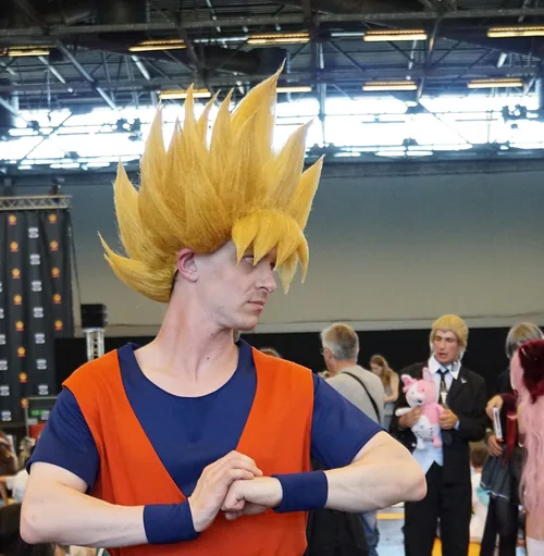 A cosplayer dressed as Goku from Dragon Ball in a golden Super Saiyan wig and an orange gi, crossing his wrists, at Japan Expo in July 2016