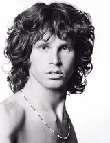 Jim Morrison with tousled dark curly hair looking at the camera in a black-and-white 1967 studio portrait