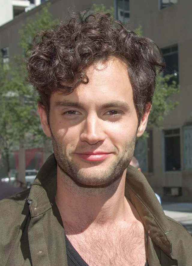 Penn Badgley, the actor who played Joe Goldberg in the series You, with tousled dark curly hair and light stubble, in an olive-green jacket over a dark shirt, photographed outdoors in September 2012