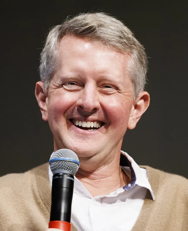 Ken Jennings laughing and holding a microphone, in a tan cardigan over a white open-collar shirt, recording an episode of the Omnibus podcast at the Library of Congress in September 2026