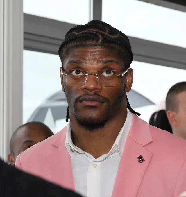 Lamar Jackson in wire-rimmed glasses and a pink blazer looking at the camera in May 2024
