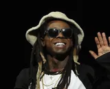 Lil Wayne smiling in sunglasses and a cream bucket hat on stage in December 2015