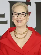 Meryl Streep smiling in black-framed glasses and a red jacket at a press conference in Seoul in April 2026