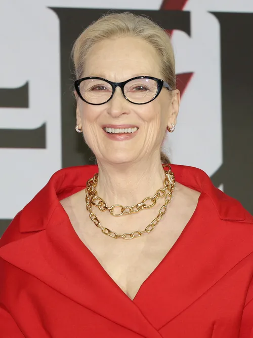 Meryl Streep smiling in black-framed glasses and a red jacket at a press conference in Seoul in April 2026