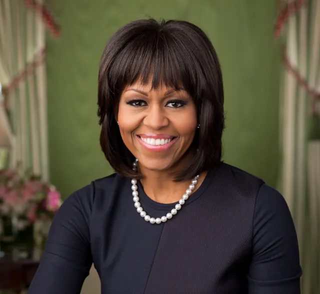 Michelle Obama smiling in a dark top with a pearl necklace, in her official White House portrait of February 2013