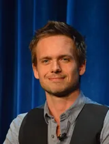 Patrick J. Adams, the actor who played Mike Ross in Suits, with tousled hair and light stubble, in a gray button-up shirt and black vest at a Suits promotional event in January 2013