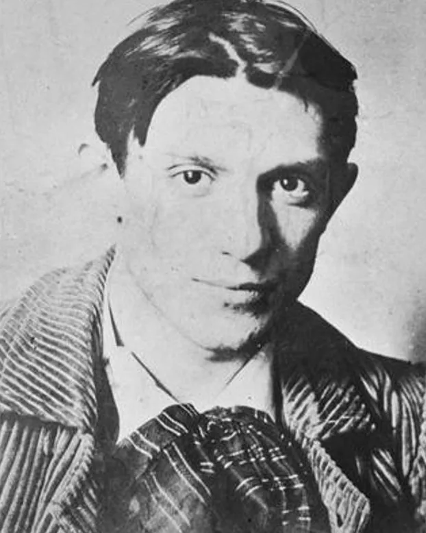 Pablo Picasso in his early twenties, with dark swept-back hair, a striped jacket and a checked neckerchief, in a photograph taken in Paris in 1904