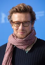 Simon Baker, the actor who played Patrick Jane in The Mentalist, smiling in tortoiseshell glasses and a pink patterned scarf at the Berlin International Film Festival in February 2020