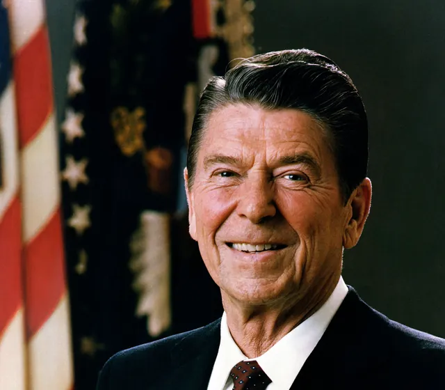 Ronald Reagan smiling in a dark suit, white shirt and maroon patterned tie, in his official presidential portrait from February 1981