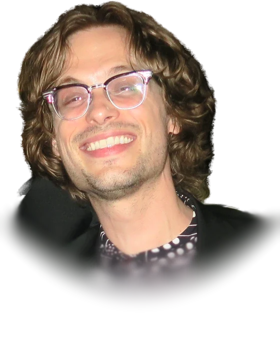 Matthew Gray Gubler, the actor who played Spencer Reid in Criminal Minds, smiling in clear-framed glasses with wavy light-brown hair, a black jacket and a black-and-white patterned shirt, in New York City in October 2017