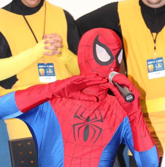 A cosplayer in the red-and-blue Spider-Man costume and full mask, speaking into a microphone at Florida Supercon in July 2013