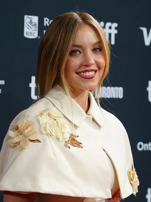 Sydney Sweeney smiling in a cream cape-sleeved jacket at the Toronto International Film Festival in September 2024