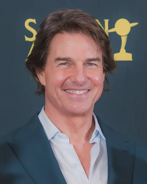 Tom Cruise smiling, with swept-back brown hair and a teal jacket over a light blue open-collar shirt, at the 53rd Saturn Awards in March 2026