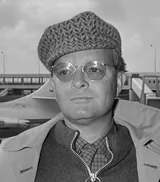 Truman Capote in round wire-rimmed glasses and a knitted cap, looking at the camera in a black-and-white photograph from March 1968