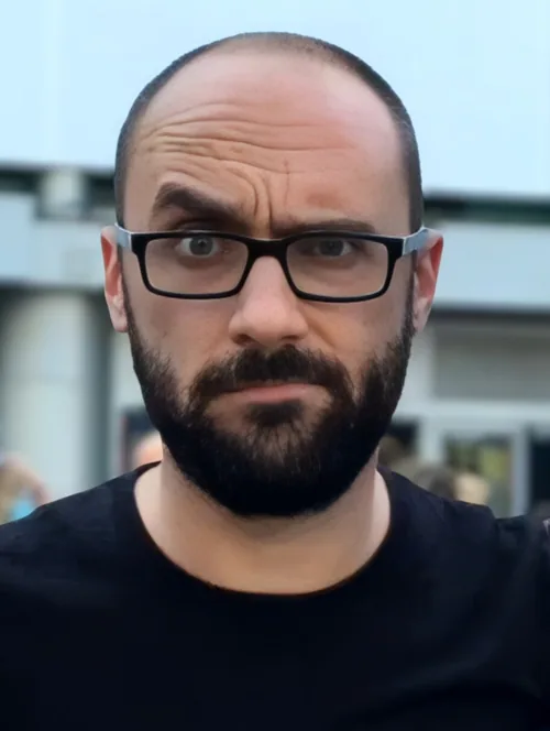 Michael Stevens, creator of the Vsauce channel, bald with a dark beard and black-framed glasses, in a black T-shirt, looking straight at the camera in July 2016